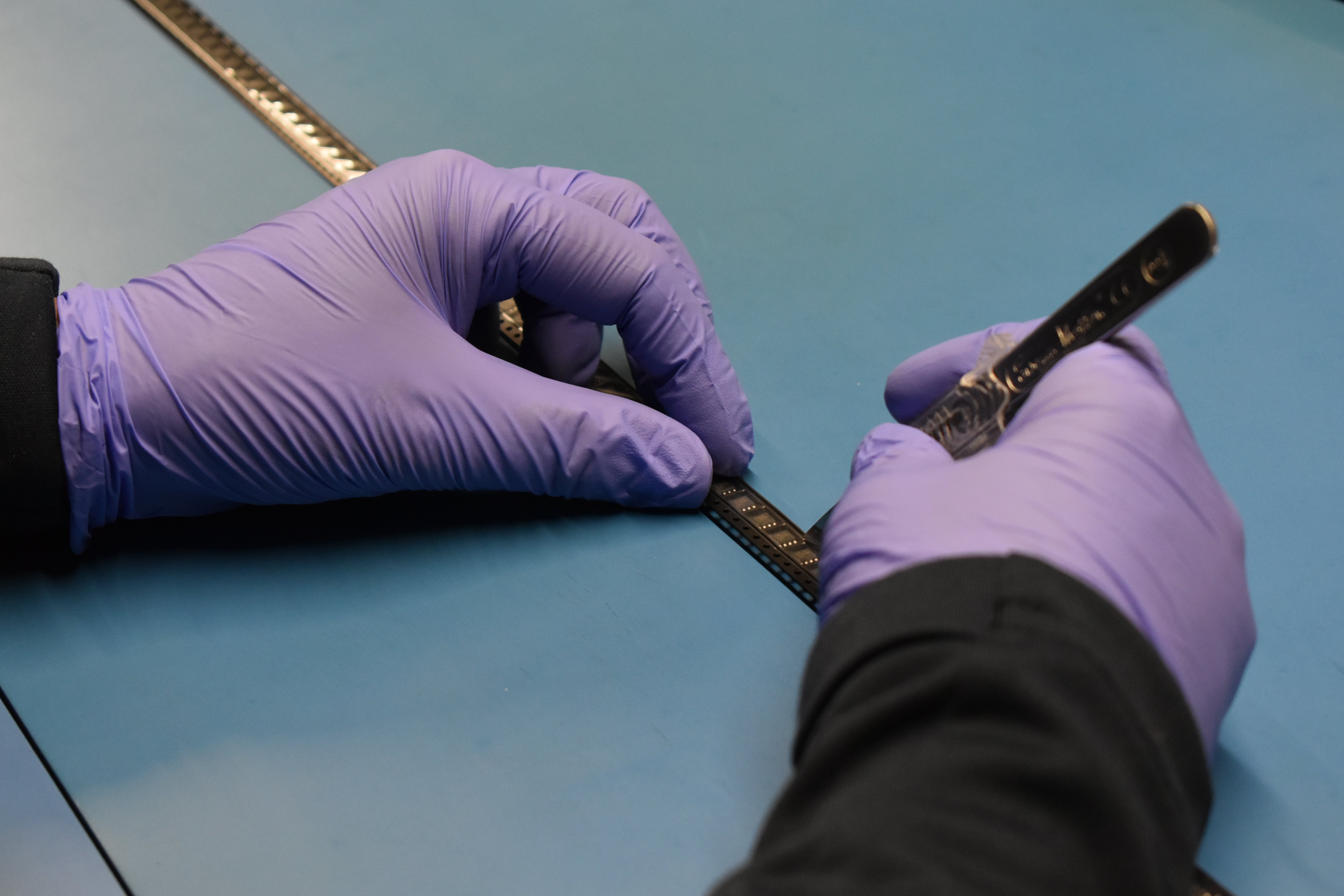 Component Sense Quality Inspector cutting into a reel of electronic components with a scalpel.