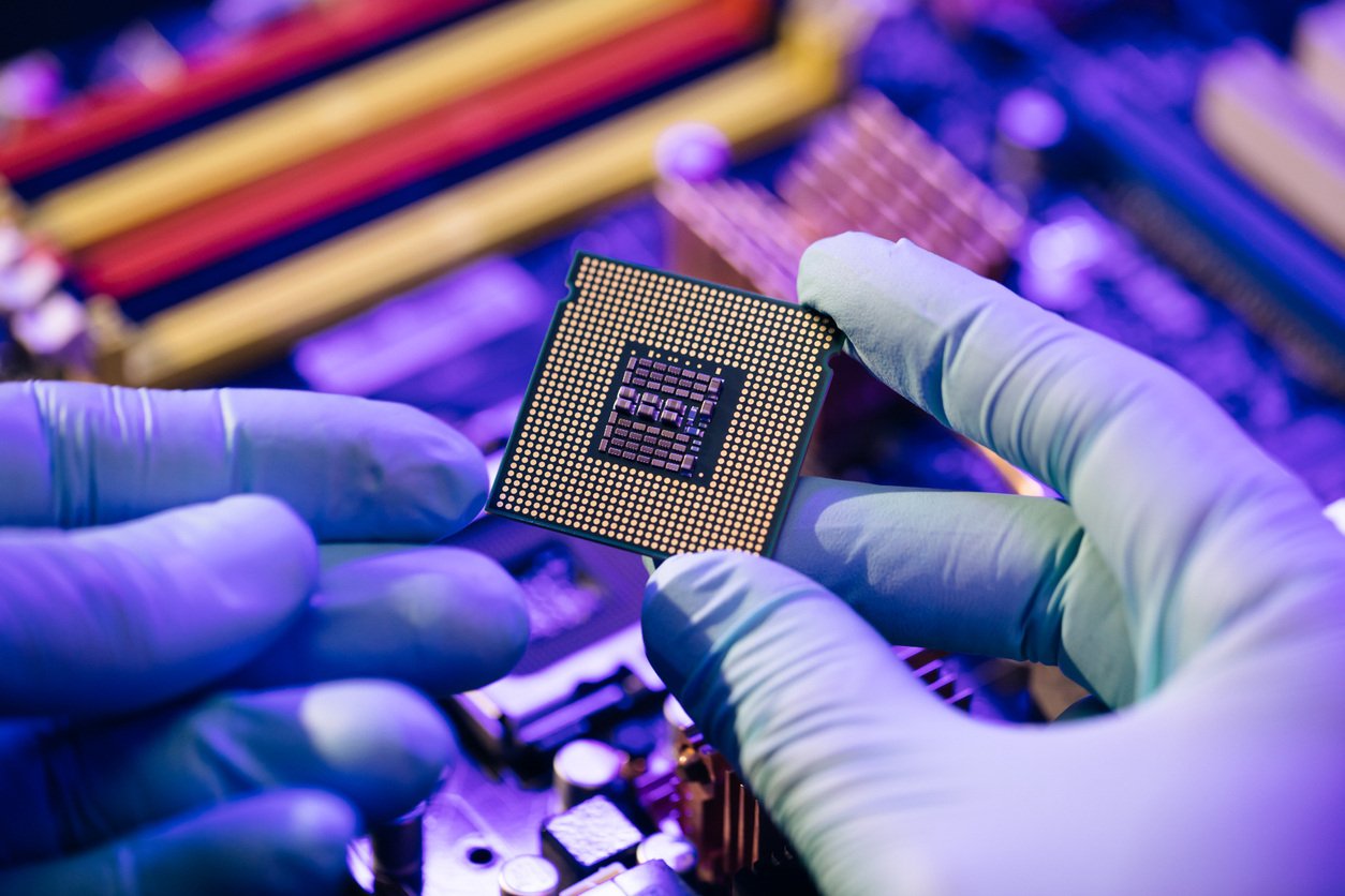 Person in purple gloves holding and inspecting an electronic component.