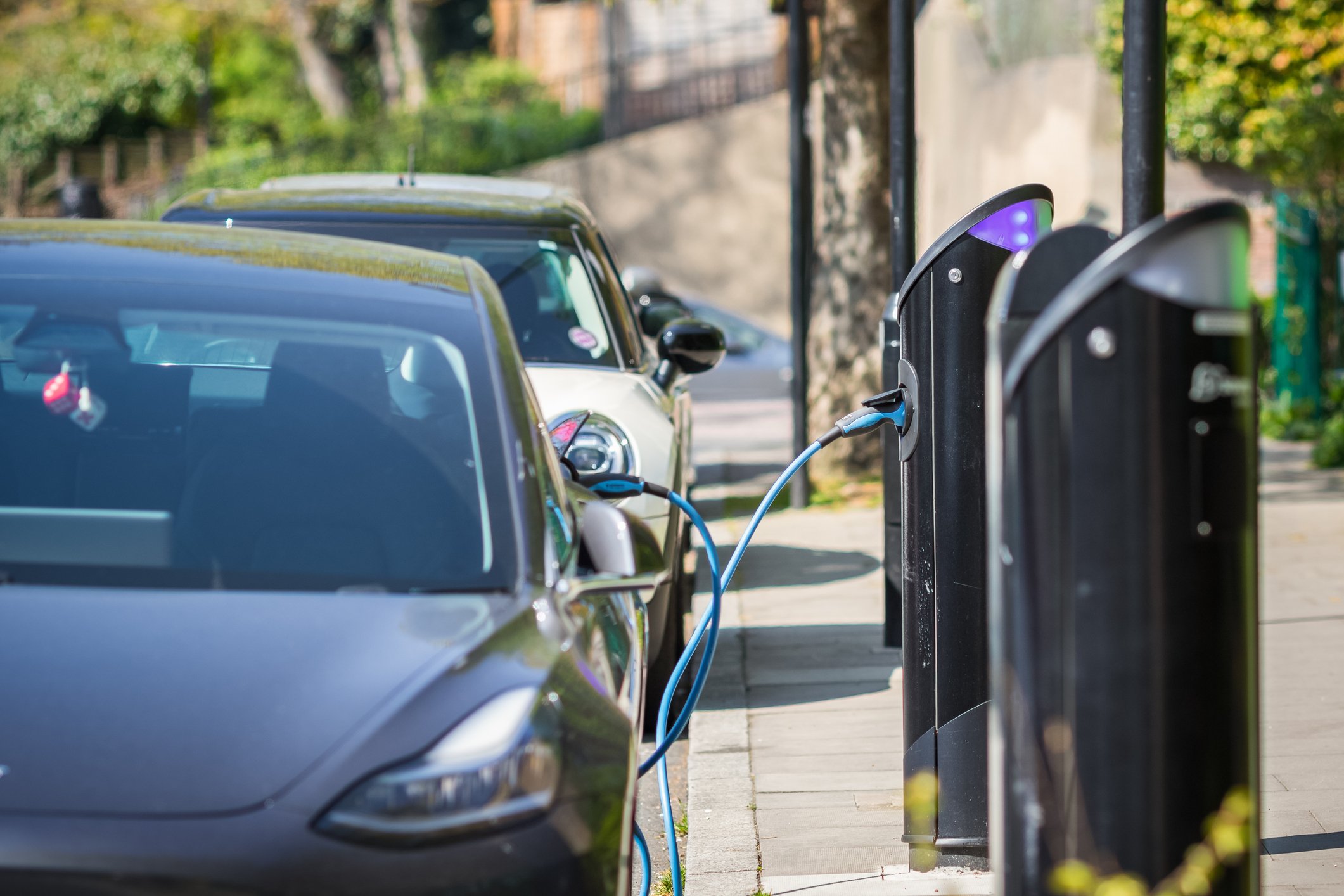 Two electronic vehicles charging at an EV charging station on the side of the road.