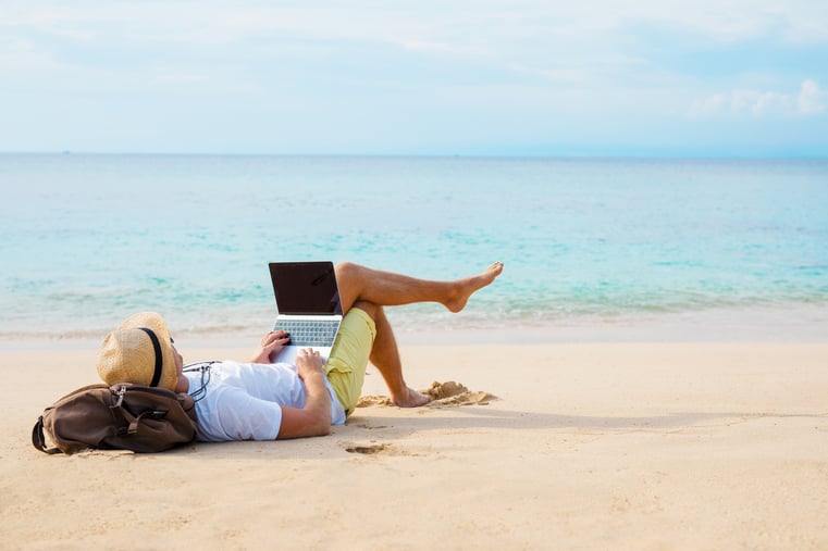 Person laying on the sand doing work on laptop.