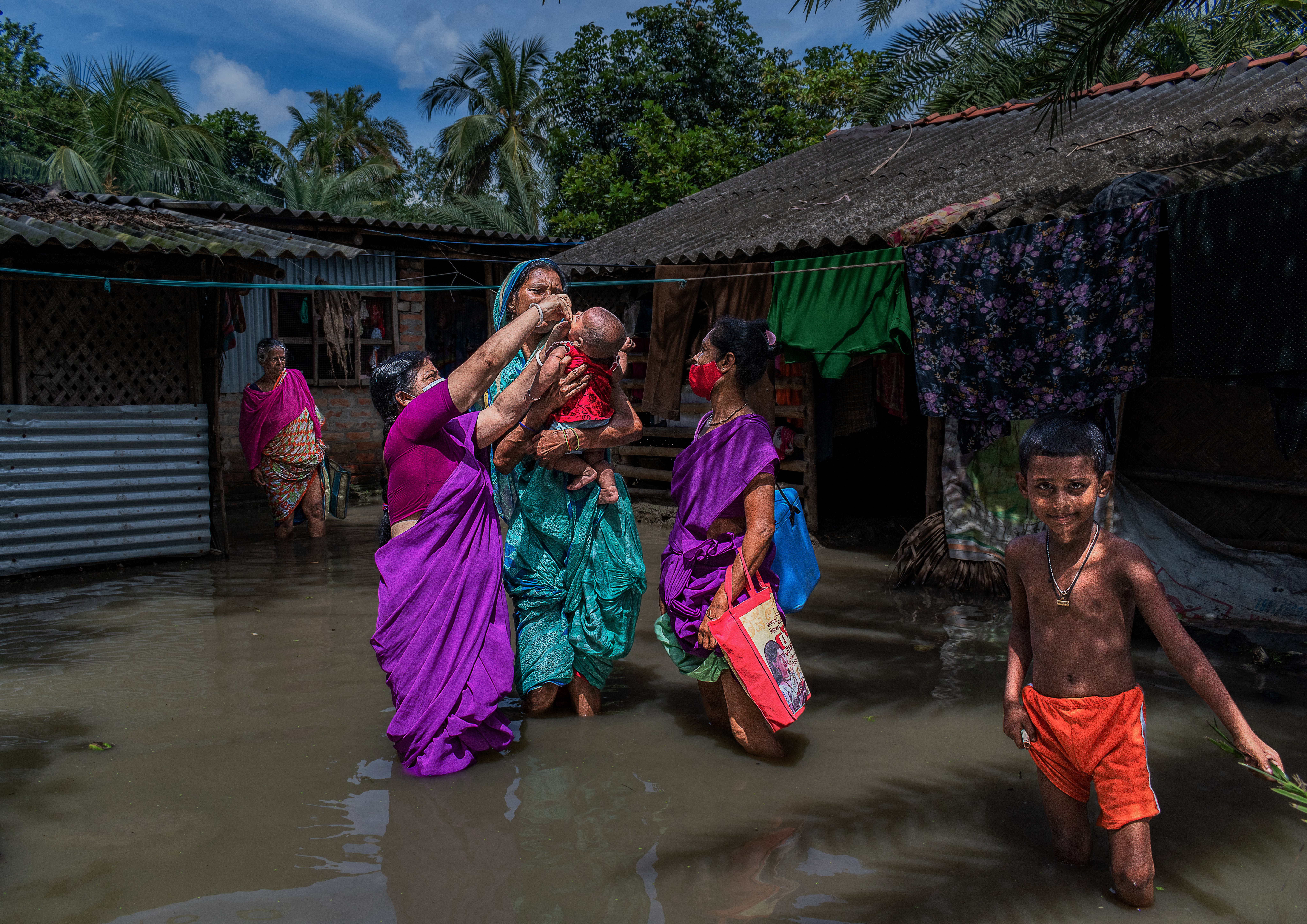 Women and children wading through water in a flooded village.